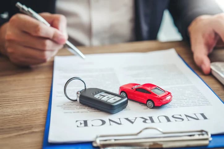 Signing an auto insurance claim document with car keys on the table